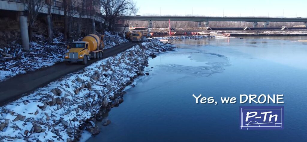 Dondlinger Construction trucks and equipment drive on a road adjacent to the river showing Bowersock Dam in Lawrence, Kansas in the background