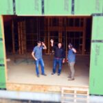 three guys standing inside a construction site wave at drone camera | P-Tn