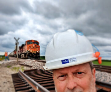 Photographer wearing construction hard hat near railroad crossing in rural area | P-Tn