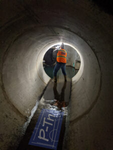 Man in orange vest in tunnel taking photo of underground sewage line | P-Tn
